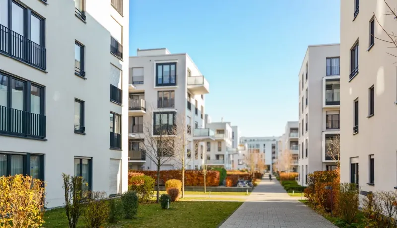 Allée pavée entre des immeubles d'habitation modernes et blancs avec de nombreux balcons et un aménagement paysager d'automne.