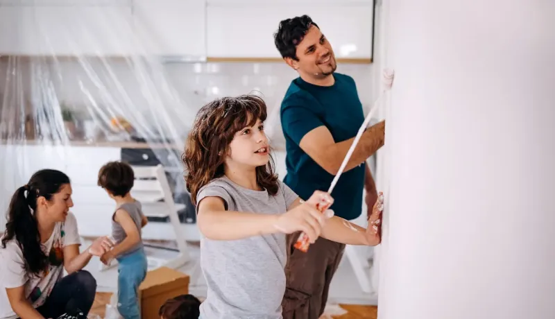 Une famille peignant un mur ensemble. Une petite fille applique de la peinture, aidée par un homme souriant.