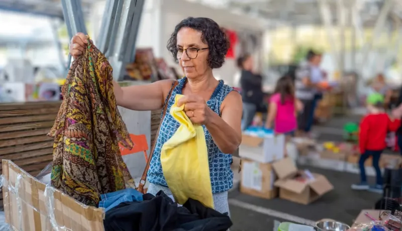 Une femme aux cheveux bouclés examine des vêtements à un marché aux puces ou dans une brocante extérieure.