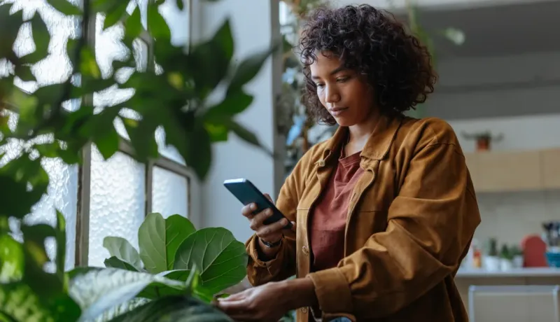 Une femme aux cheveux bouclés prend une photo d'une de ses plantes d'intérieur avec son téléphone.