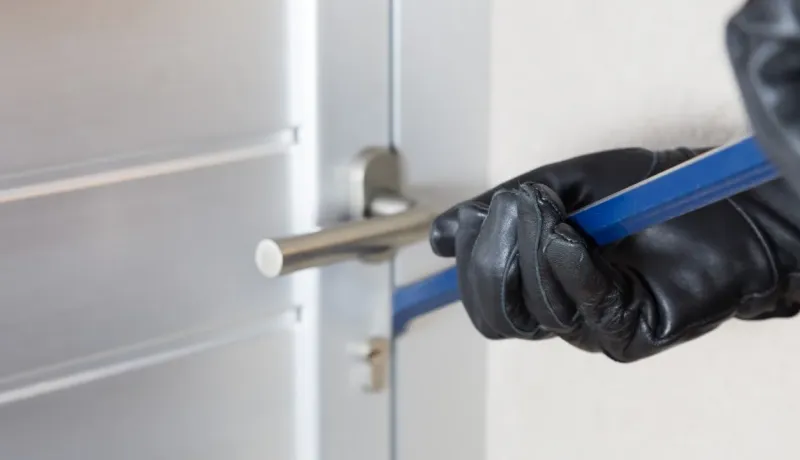 Gros plan sur une main gantée de noir utilisant un pied-de-biche pour forcer une porte moderne.