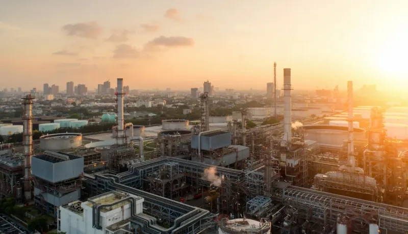 Vue aérienne d'une raffinerie ou complexe industriel en milieu urbain, au coucher du soleil.