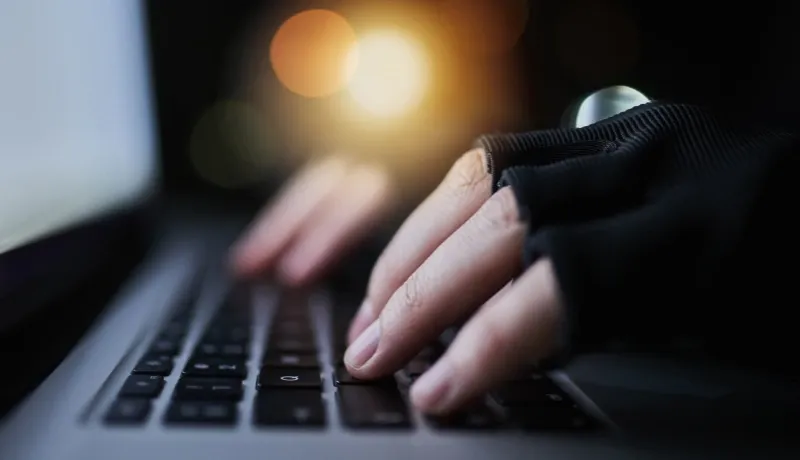 Gros plan sur des mains gantées tapant sur un clavier d'ordinateur dans l'obscurité.