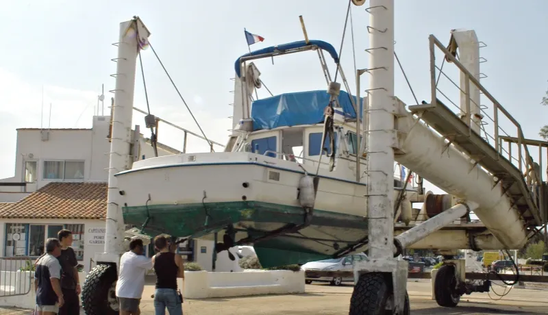 Bateau de plaisance blanc soulevé par un chariot élévateur de mise à l'eau dans un port de plaisance.