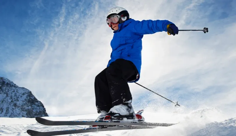 Jeune skieur en pleine action réalisant un saut sur une piste enneigée sous un ciel bleu vif.