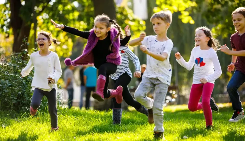Un groupe d'enfants joyeux court et s'amuse sur une pelouse ensoleillée dans un parc verdoyant.