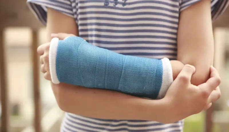 Gros plan sur un enfant portant un plâtre bleu au bras, illustrant un soin après une blessure.