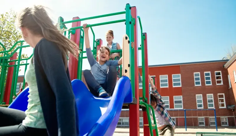 Des enfants rient et s'amusent sur une structure de jeux colorée avec toboggan dans une cour d'école.