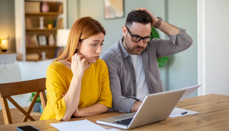Un couple regarde l’écran d’un ordinateur, avec des documents papier à côté.