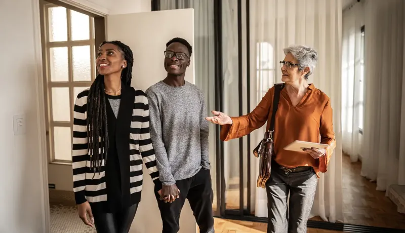 Trois personnes visitent une maison, l'agent immobilière montre quelque chose du doigt.