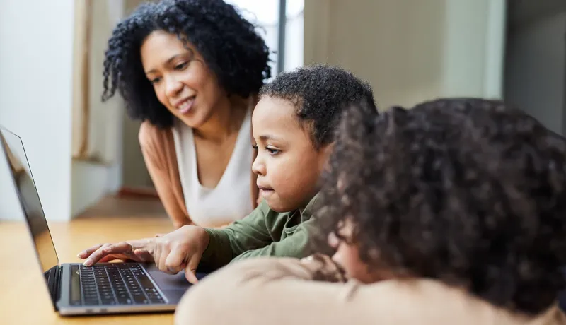 Une mère supervise ses deux enfants qui regardent un ordinateur portable ensemble.