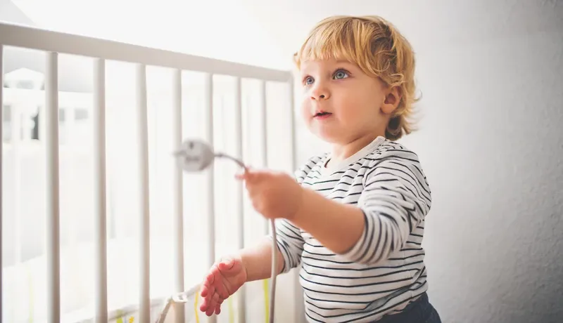 Un enfant en bas âge tenant un câble électrique dans sa main devant un lit à barreaux.