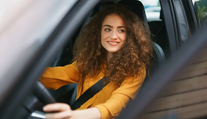 Une jeune conductrice souriante au volant de sa voiture.