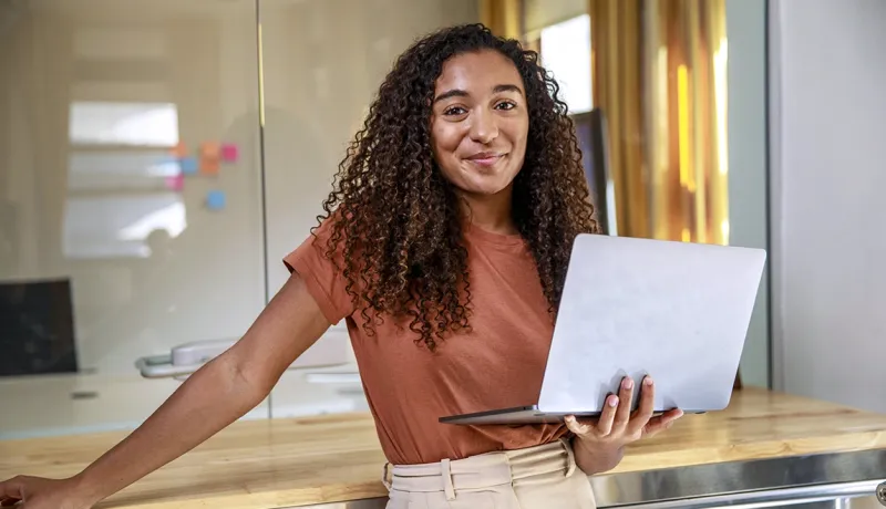 Une jeune femme en contrat d'alternance tient un ordinateur portable, prête à travailler dans un environnement professionnel.