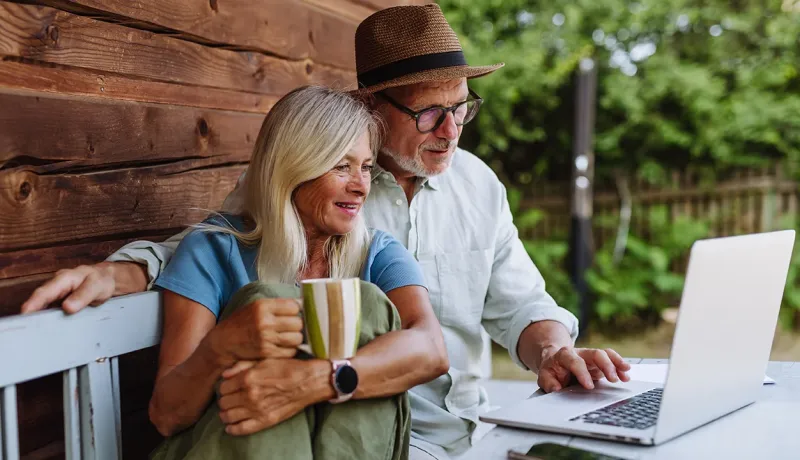Un couple de seniors utilise leur ordinateur dans leur salon de jardin.