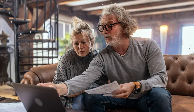 Un couple de seniors consulte des documents et utilise leur ordinateur dans leur salon.