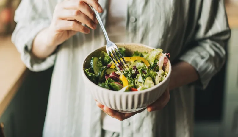 Gros plan sur une personne tenant un bol de salade colorée et fraîche. Elle est prête à manger sa salade à la fourchette.