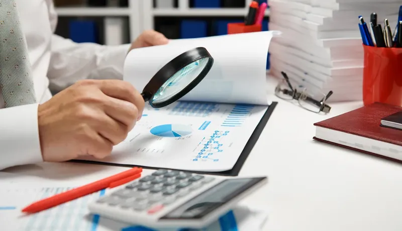 Un professionnel examine des documents avec une loupe.