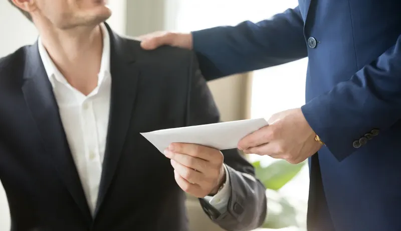 Un homme en costume remet une enveloppe à un autre homme, symbolisant un échange professionnel.