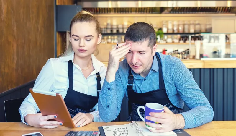 Un couple de professionnels assis à une table, examinant des comptes financiers sur des documents.