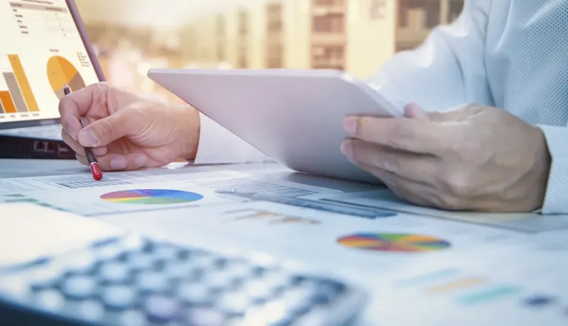 Un professionnel analyse des données financières sur un ordinateur portable et une tablette, entouré de graphiques.