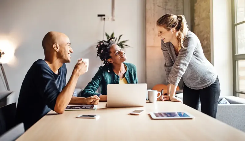 Trois salariés souriants discutent autour d'une table.