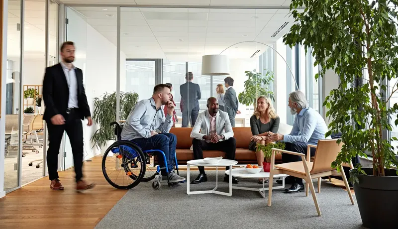 Groupe de collègues discutant de façon inclusive dans un espace de coworking, dont un homme en fauteuil roulant.