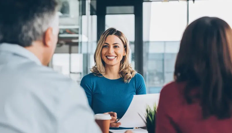 Une femme souriante en haut bleu participe activement à une réunion d'équipe professionnelle au bureau.