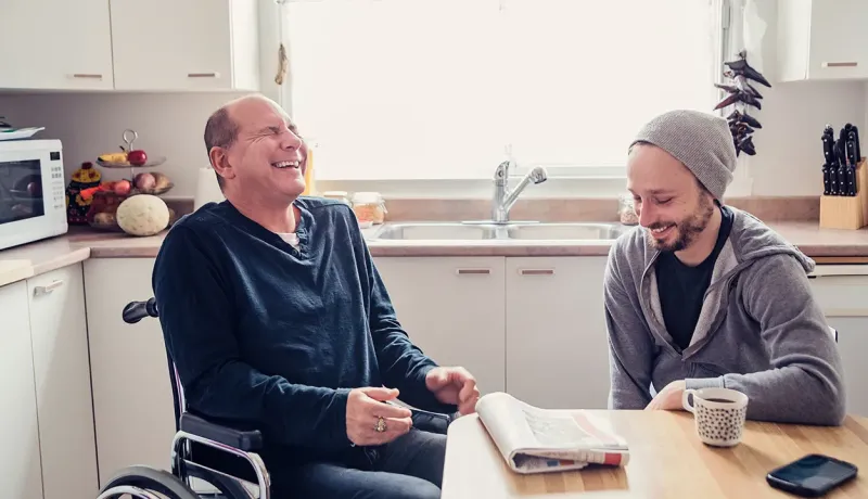 Deux hommes assis à une table dans une cuisine, discutant et partageant un moment convivial.