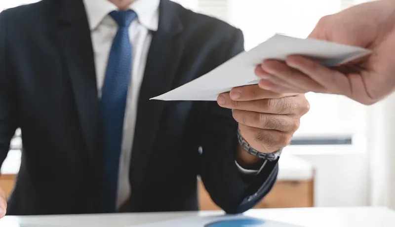 Personne en costume tendant une enveloppe à une autre personne.