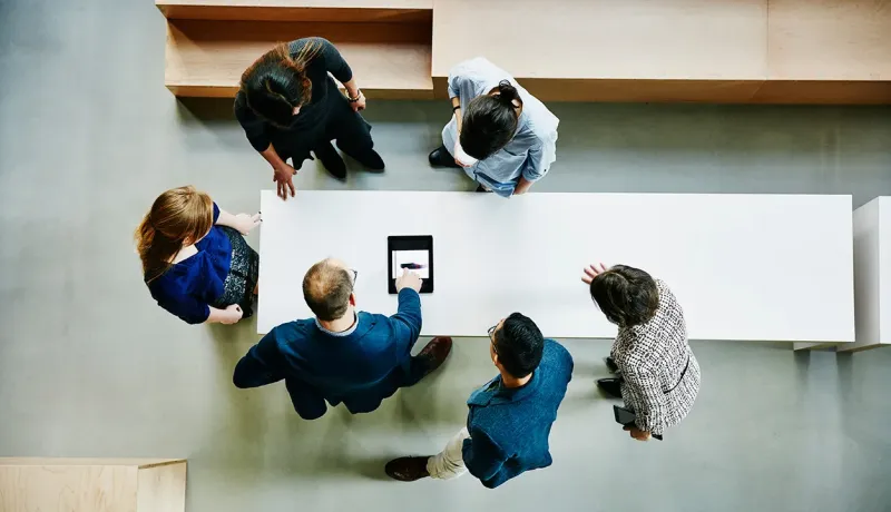 Groupe de collaborateurs réunis autour d'une table, vu du dessus.