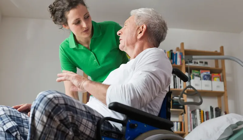Une femme en chemise verte aide un homme âgé dans un fauteuil roulant