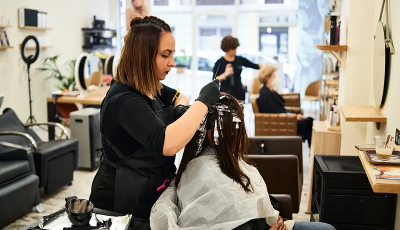 Une femme se fait coiffer dans un salon de beauté, assise sur une chaise avec un coiffeur à ses côtés.