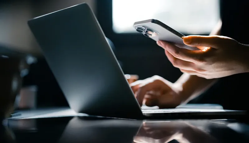 Une personne utilise un téléphone portable tout en travaillant sur un ordinateur portable