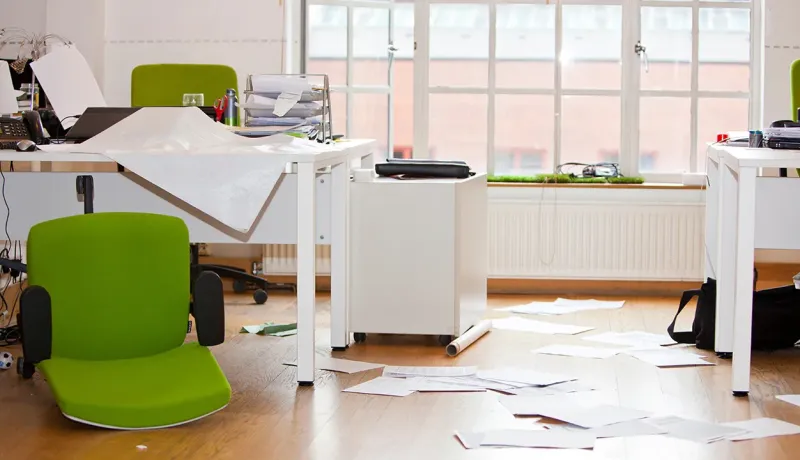 Espace de travail chaotique, comprenant un bureau désorganisé et plusieurs chaises en désordre.