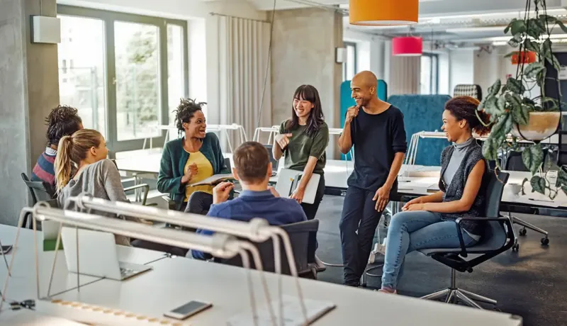 Groupe de collègues souriants échangeant de manière conviviale dans un espace de coworking lumineux.