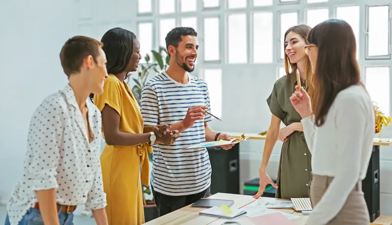 Collaborateurs de bureau discutant joyeusement autour d'une table de réunion avec un document.