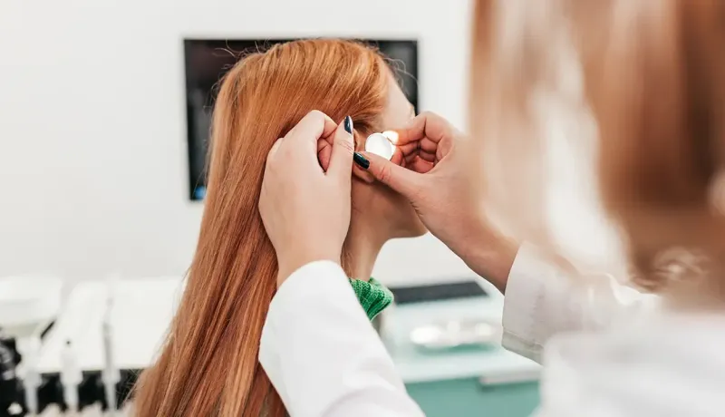 Une professionnelle de santé examine l'oreille d'une patiente rousse avec un otoscope éclairé.