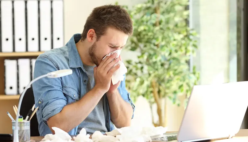 Homme qui se mouche devant un ordinateur